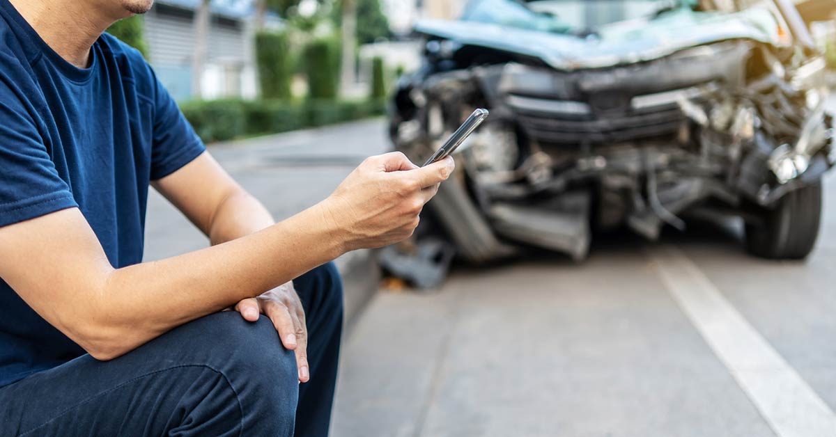 male driver checking phone if he has gap insurance after a car accident