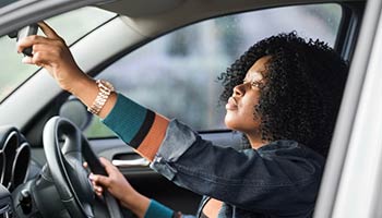 Woman adjusting her rear view mirror to be a good driver in order to qualify for an auto insurance discount. 