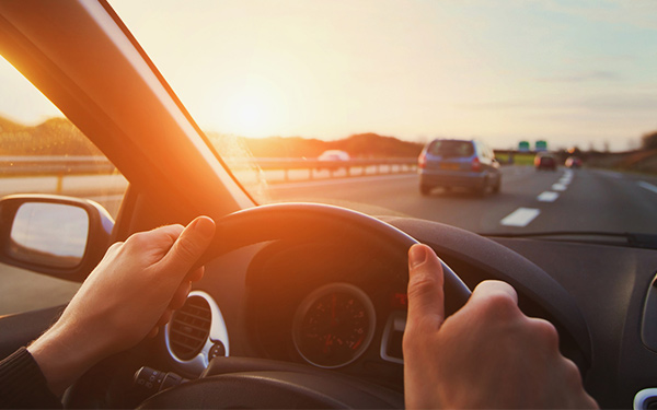 Image shows a person with their hands on a steering wheel driving down the road.