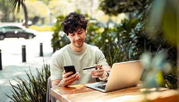 Image shows a young person on their phone paying a credit bill. 