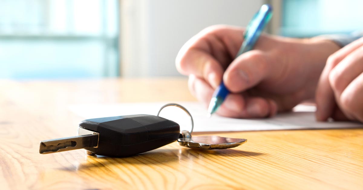 Person signing car rental documents in order to rent a car. Keys are on the table.
