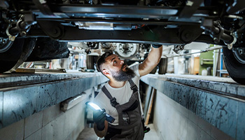 Body shop repair employee working underneath a car.