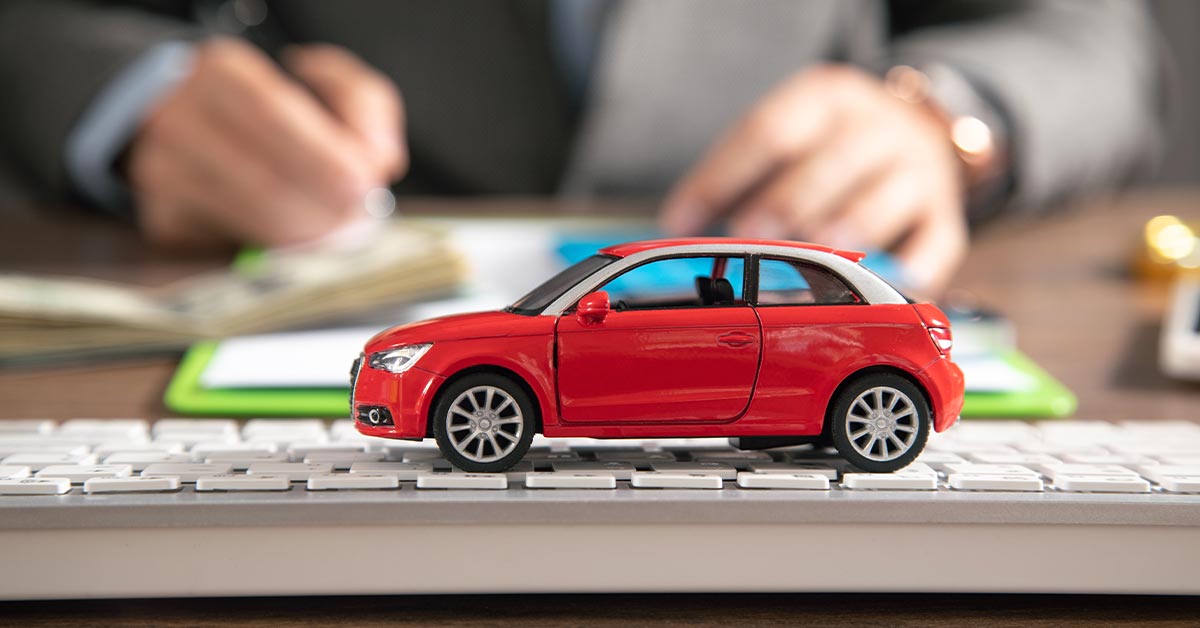 a toy car in front of an auto insurance agent signing a paper