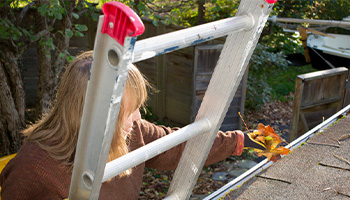 A woman standing on ladder cleaning her gutters