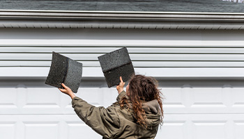 A person standing outside their home performing a roof inspection holding up roof shingles