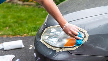 a person performing diy car maintenance by restoring their headlights