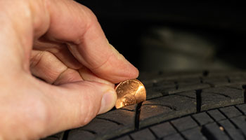 a person using a penny to check the tread on their car tires