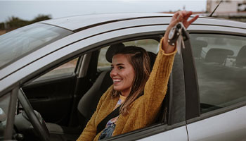 a newly licensed young driver holding up the keys to their new car