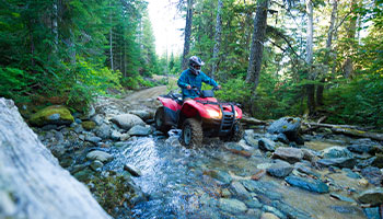 person riding an atv through a shallow creek