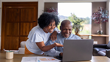 happy senior couple at home smiling at their computer as they shop for car insurance online, 