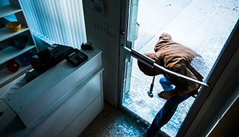 burglar breaking into a small business front door with glass shattered on floor