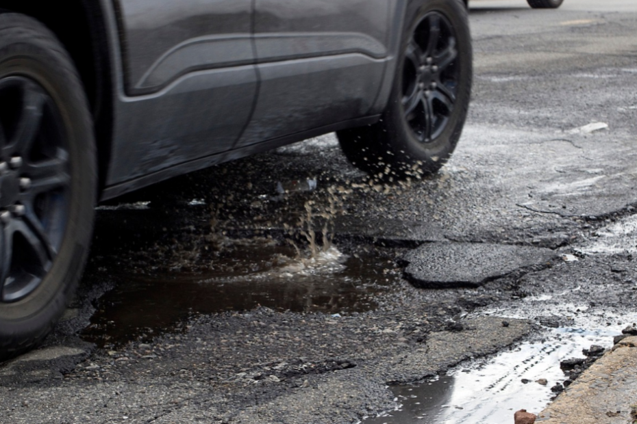 a car driving over a pothole trying to avoid damage to their car. pothole has water and is deep