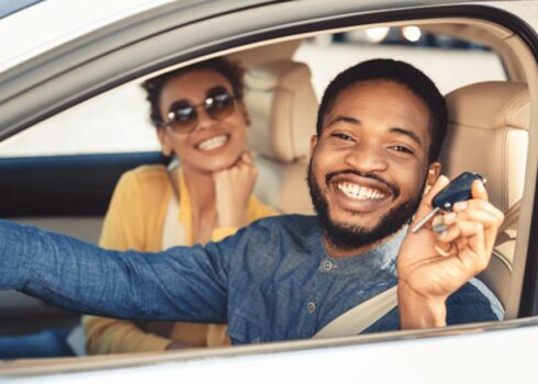 A couple inside of a car smiling. Young man is holding car keys in his hand.